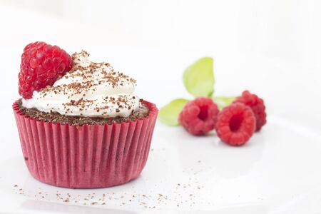 Chocolate cupcake topped with icing and a raspberry sprinkled with chocolate, raspberries in the...