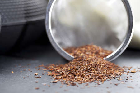 Dried rooibos tea leaves beside teapot の写真素材