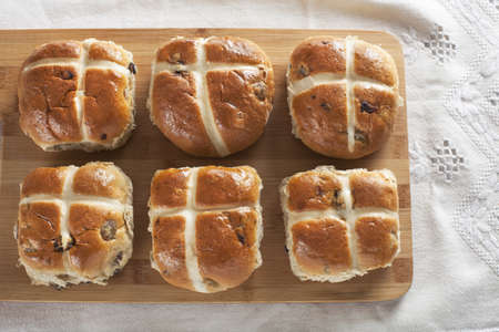 Six hot cross buns on a wooden cutting board