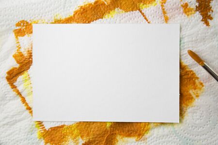 Blank white watercolor paper on towel with orange paint and paintbursh covered with orange paint.の写真素材