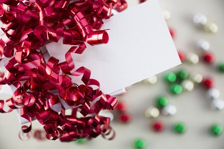 Red curly ribbons on gift box and gift tag with copy space, ornaments out of focus in background.の写真素材