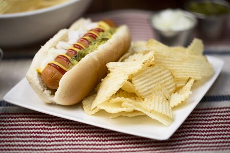 Veggie hot dog topped with mustard, ketchup, onions and relish, served with potato crisps (chips).