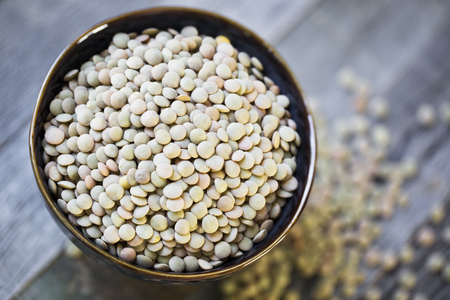 Fresh dried green lentils in ceramic bowl set on wooden tableの写真素材