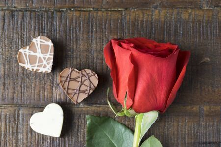 Bright red rose and three heart shaped chocolatesの写真素材