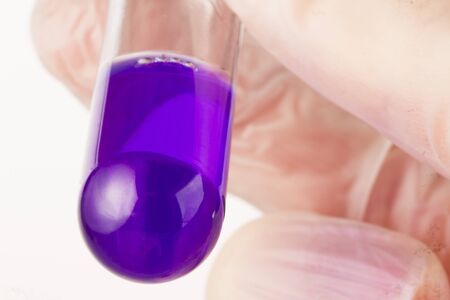 Close up of fingers holding test tube containing purple liquid.の写真素材