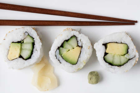 Vegan cucumber and avocado uramaki sushi rolls with wasabi, pickled ginger, and chop sticks.の写真素材