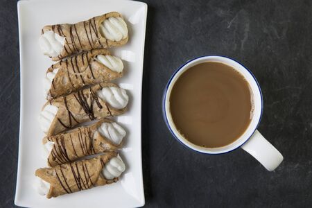 Pastries Stuffed with sweet cream and drizzled with chocolate and a cup of tea or coffee, viewed from above.の写真素材