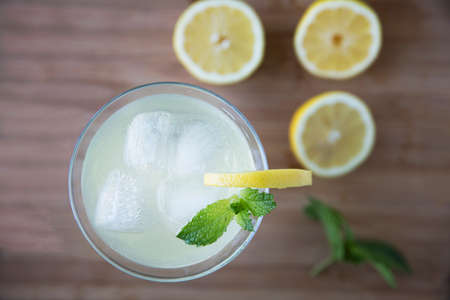 Top view of refreshing lemon drink garnished with mint and out of focus lemons on tableの写真素材