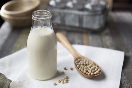 Homemade soy milk in glass bottle with soybeans in wooden spoonの写真素材