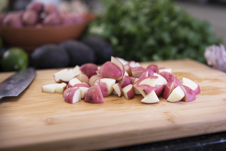 Red potatoes cut in halves and quarters on cutting board in kitchen.の写真素材