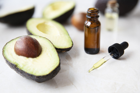 Small bottle with dropper of avocado oil and avocados on marble surface.の写真素材