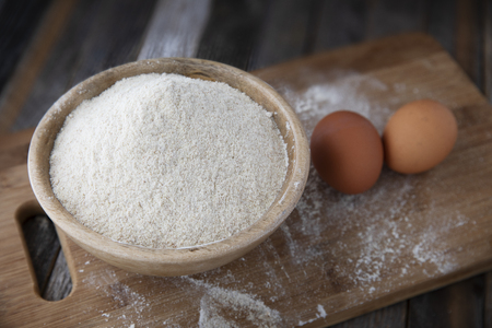Bowl of whole wheat flour and two eggs on a cutting board.の写真素材