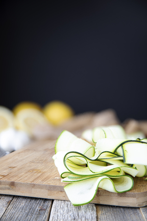 Fresh zucchini sliced into ribbons and sitting on wooden cutting board with copy space at top.の写真素材
