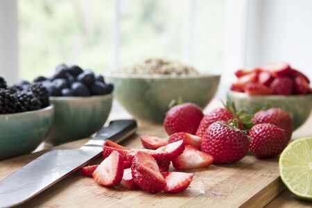 Sliced and whole strawberries on cutting board with knife, horizontal orientation.