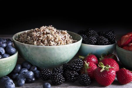 Bowl of healthy quinoa and fresh berries in green bowls, low key lighting and horizontal orientation