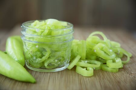 Fresh sliced banana peppers on a cutting board with jar ready for pickling.