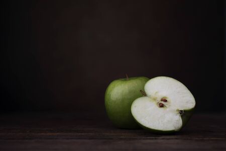 Two granny smith apples, one whole and one cut in half.  Two granny smith apples with old pottery jug.  Shot at eye level with dark rustic feel and copy space/の写真素材