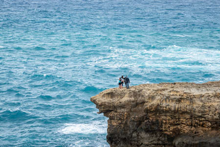Group of Tourist people taking selfie on the edge of a cliff in Gozo during winter with a selfie stick. danger spot on rough seaの写真素材