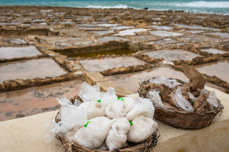 Salinas. Salt Pans or salters at the background with salt bags ready for sale in a basket or bowl outdoor. Hand harvest salt in Gozo Island Marsalforn. space for text.の写真素材