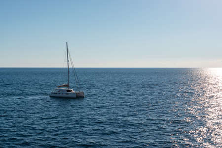 White Sailing boat in Malta traveling to Gozo on a bright sunny summer day in the middle of nowhere. catamaran sailing boat. no sails up in calm sea.の写真素材