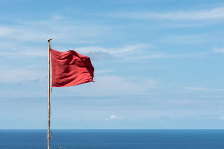 Red flag waving on a pole. Clouds and sea view background. Horizontal Viewの写真素材