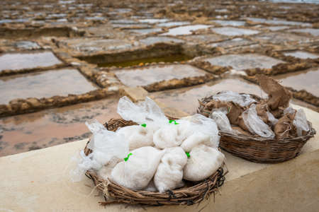 Salinas. Salt Pans or salters at the background with salt bags ready for sale in a basket or bowl outdoor. Hand harvest salt in Gozo Island Marsalforn. space for text.の写真素材