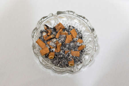 Cigarette stubs and ash in a glass ashtray. Isolated white background. Horizontal. above viewの写真素材