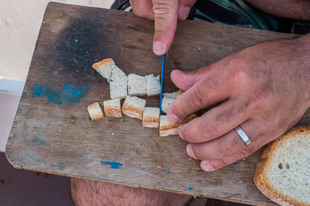 Married Fisherman Preparing or cutting bread For Fishing Bait on a piece of wood With a knife while underway on a boat. Horizontal. closeup. space for text.の写真素材