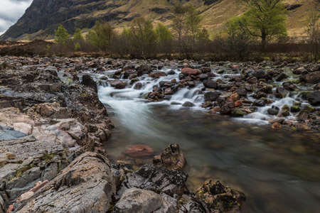 Glencoe river with smooth water flow and cloudy day. hill views at the backの写真素材