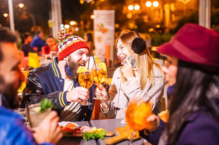Man and woman smiling and toasting at winter cocktail bar outdoors wearing open face mask - New normal lifestyle concept with millennial people having fun together - Focus on blond girlの写真素材