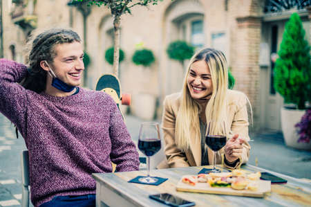 Couple drinking red wine at bar with open face masks in coronavirus time - New normal concept - Focus on womenの写真素材