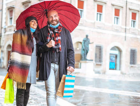 Romantic happy couple hugging under an umbrella while walking on the street with shopping bag in the covid-19 time - New normal seasonal sales time concept - Cold filterの写真素材