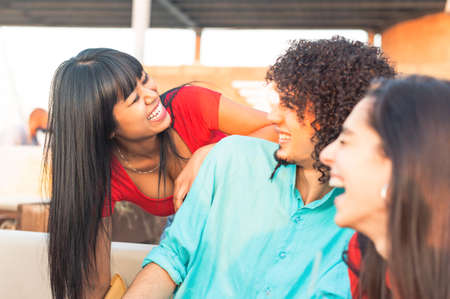 Beautiful happy thai girl at bar laughs loudly with multiracial young friends - Cheerful multi ethnic friends talking in patio in the summer time - Focus on smile girlの写真素材