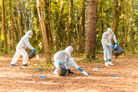 Workers in protective suit with face masks, collects dirty medical protections for covid-19 in a park - Ecology concept and mindfulness after coronavirus pandemicの写真素材