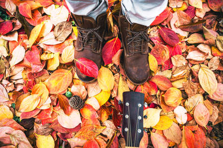 Autumn fall concept with colorful leaves and brown boots outside - Close up of man feet and guitarの写真素材