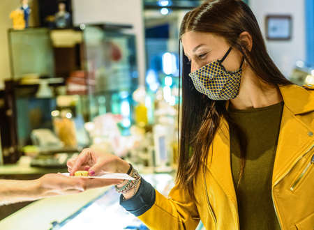 Happy female customer with face mask, taking one chocolates from man or barman at pastry - Good dessert - New normal lifestyle concept about sweet life in covid-19 timeの写真素材