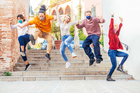 Happy crazy friends with face mask jumping down the stairs in the city street in corona virus time -...