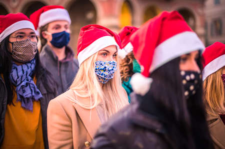 Merry Christmas! Friends group walking at city wearing face mask and santa hat in coronavirus time -...