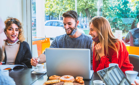 Happy friends with face mask talking and having fun with video call in the laptop - Young people at coffee shop drinking coffee and cappuccino - New normal smart working lifestyle conceptの写真素材