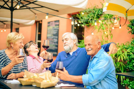 Senior people laughing and toasting red wine at restaurant - Friendship concept with happy mature friends having fun together at home in the gardenの写真素材