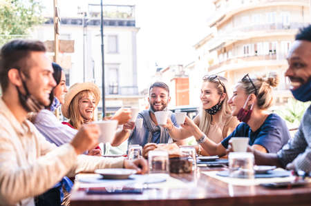 Friends having fun drinking and eating at coffeehouse with face mask- Young people talking together at restaurant cafeteria in covid time - New normal lifestyle concept with happy men and womenの写真素材