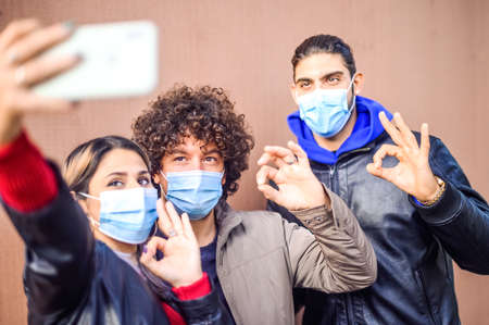 Self portrait of happy positive friends shooting selfie on front camera showing ok, like sign with fingers - New normal lifestyle concept about happy students in pandemic timeの写真素材
