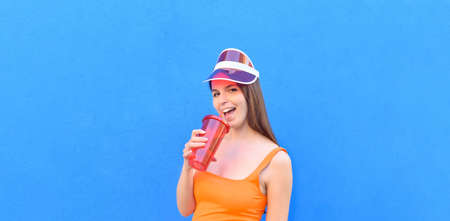 Portrait young beautiful sexy woman with cap, drinks through a straw from a red glass as he makes a winking face - Sexy, joy, concept about happy girl in summer trip - space for advertisingの写真素材