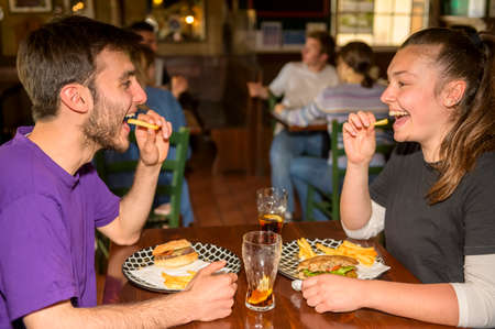 Boy and girl eat French fries while they look into each other's eyes and laugh - Young teenagers...