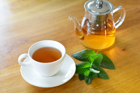White ceramic cup and glass teapot of herbal tea with fresh mint twig on wooden tableの写真素材