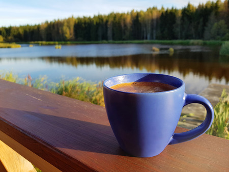 Cup of fresh aromatic coffee by a lake in the morningの写真素材