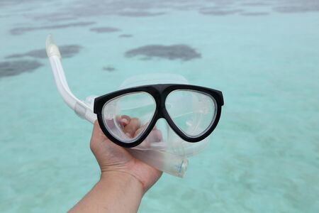 background of hand holding a diving mask and a snorkelの写真素材