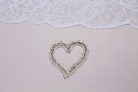 background of wave on a sand with heart drawingの写真素材