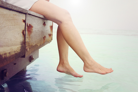 Woman's legs hanging  into the sea on wooden pierの写真素材