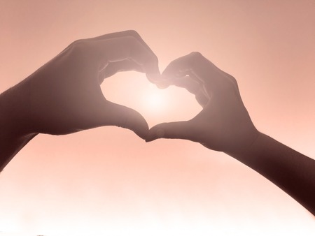 heart shape making of hands against the sunの写真素材